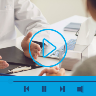 Physician talking to patient at desk. Video play button on top of image.